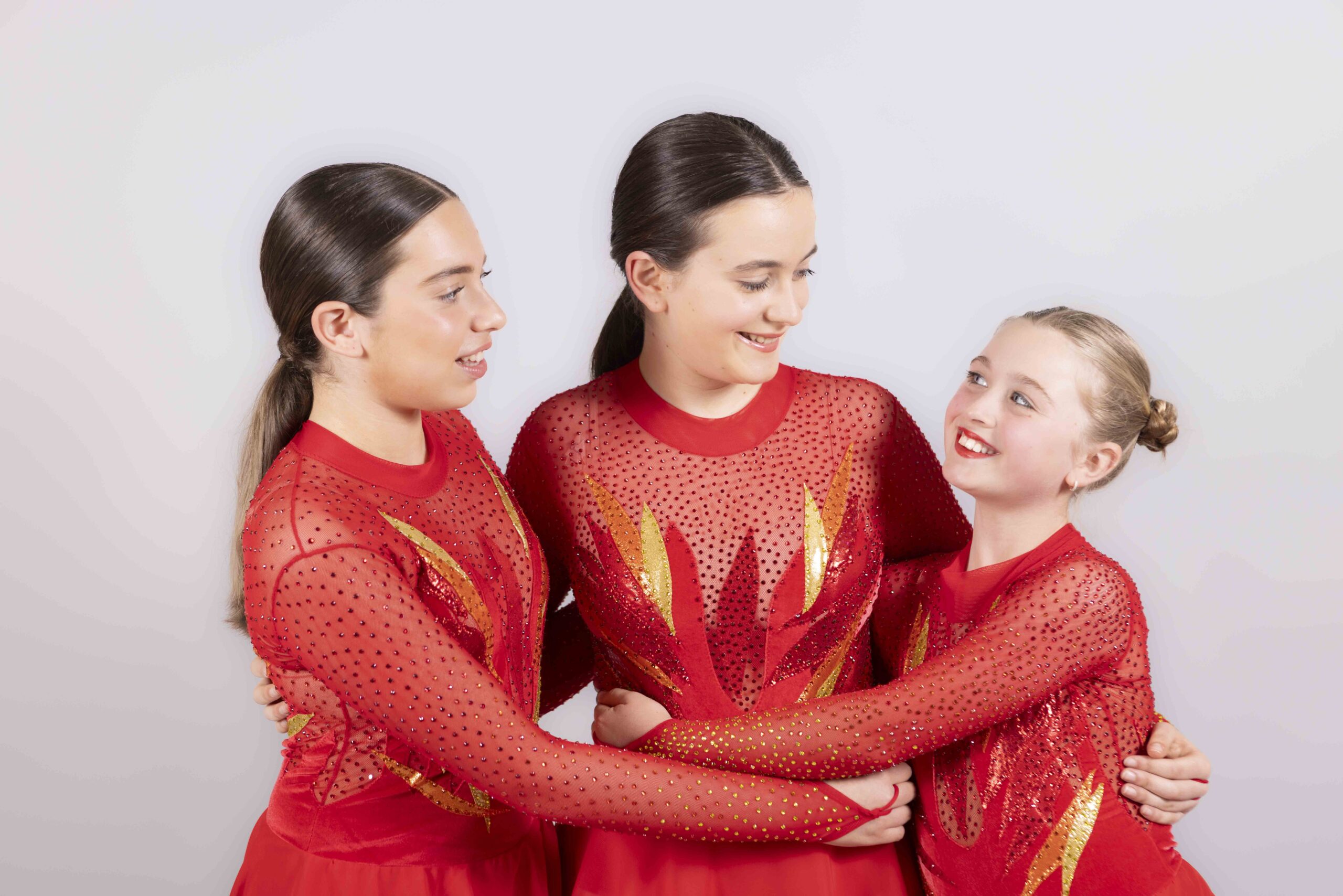 Three LBSD pupils smiling together in red dance costumes
